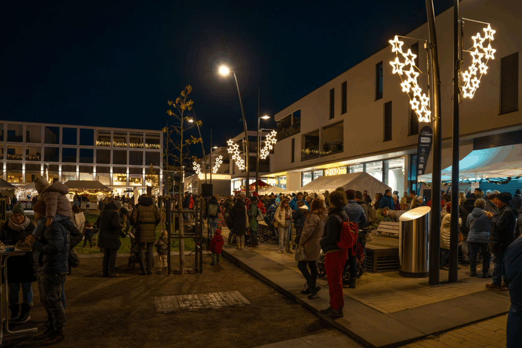Belebter Nachtmarkt mit festlicher Beleuchtung und Menschenmengen in einer modernen urbanen Umgebung.