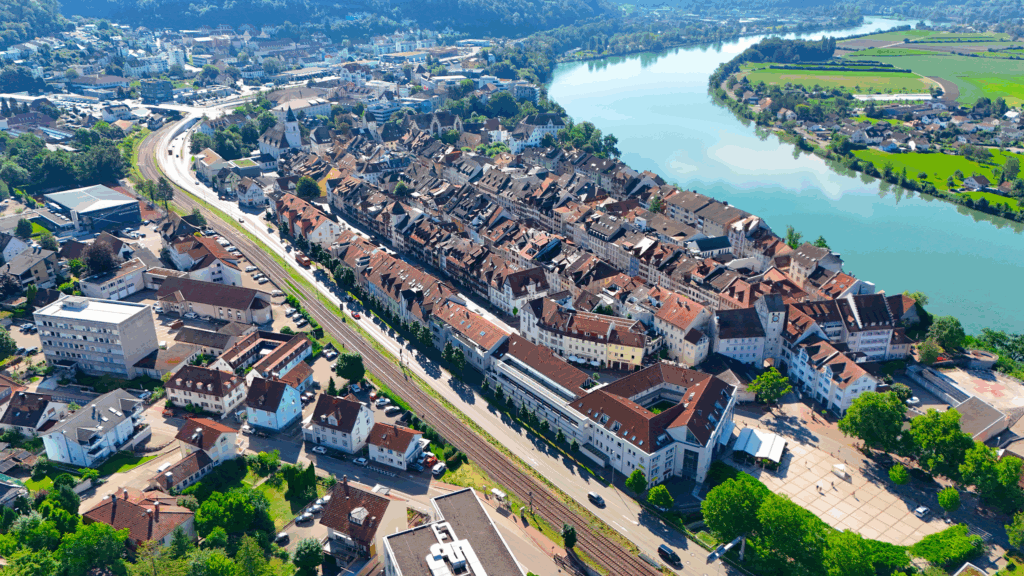 Luftaufnahme einer Stadt mit Farbenfrohen Häusern, einem Fluss und einer umgebenden Landschaft.